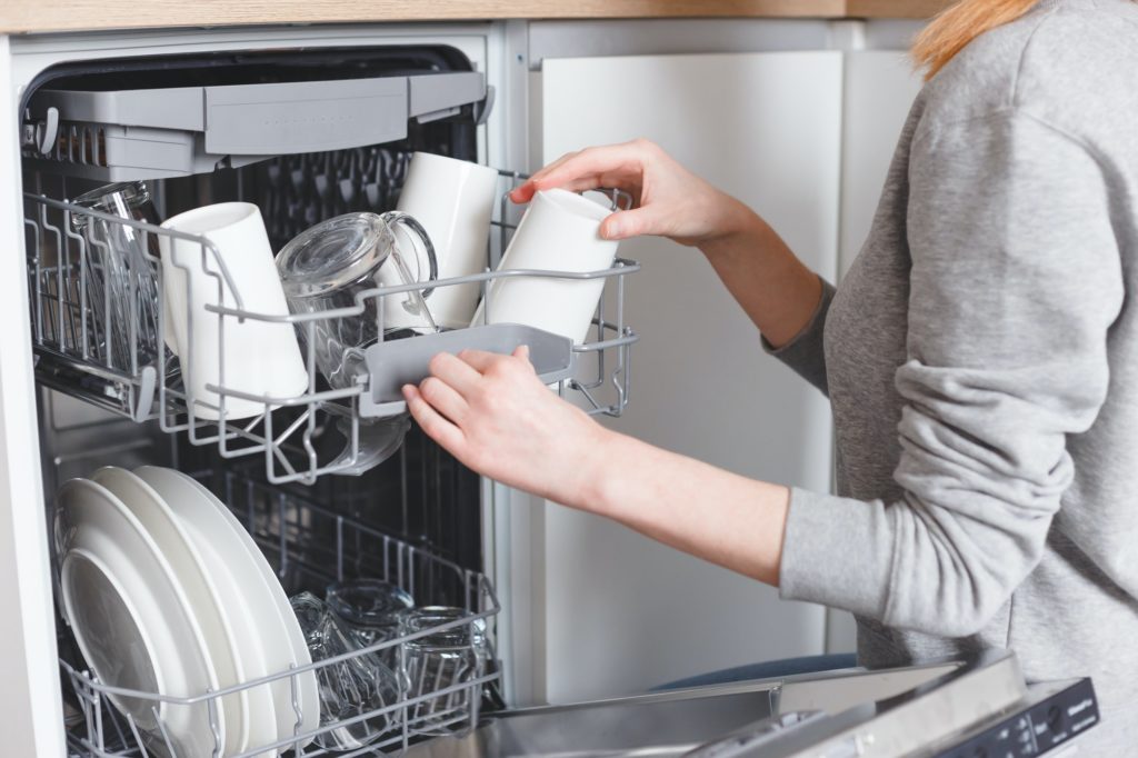 Housework: young woman putting dishes in the dishwasher